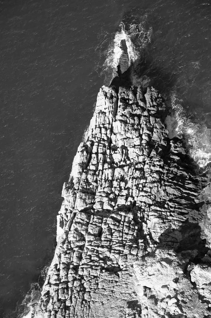 Steile Felsformation im Meer aus der Luft in Schwarz-Weiß